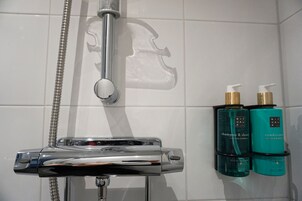 Un baño con cabezal de ducha cromado, ducha de mano y dos botellas de champú y acondicionador en un estante de pared.