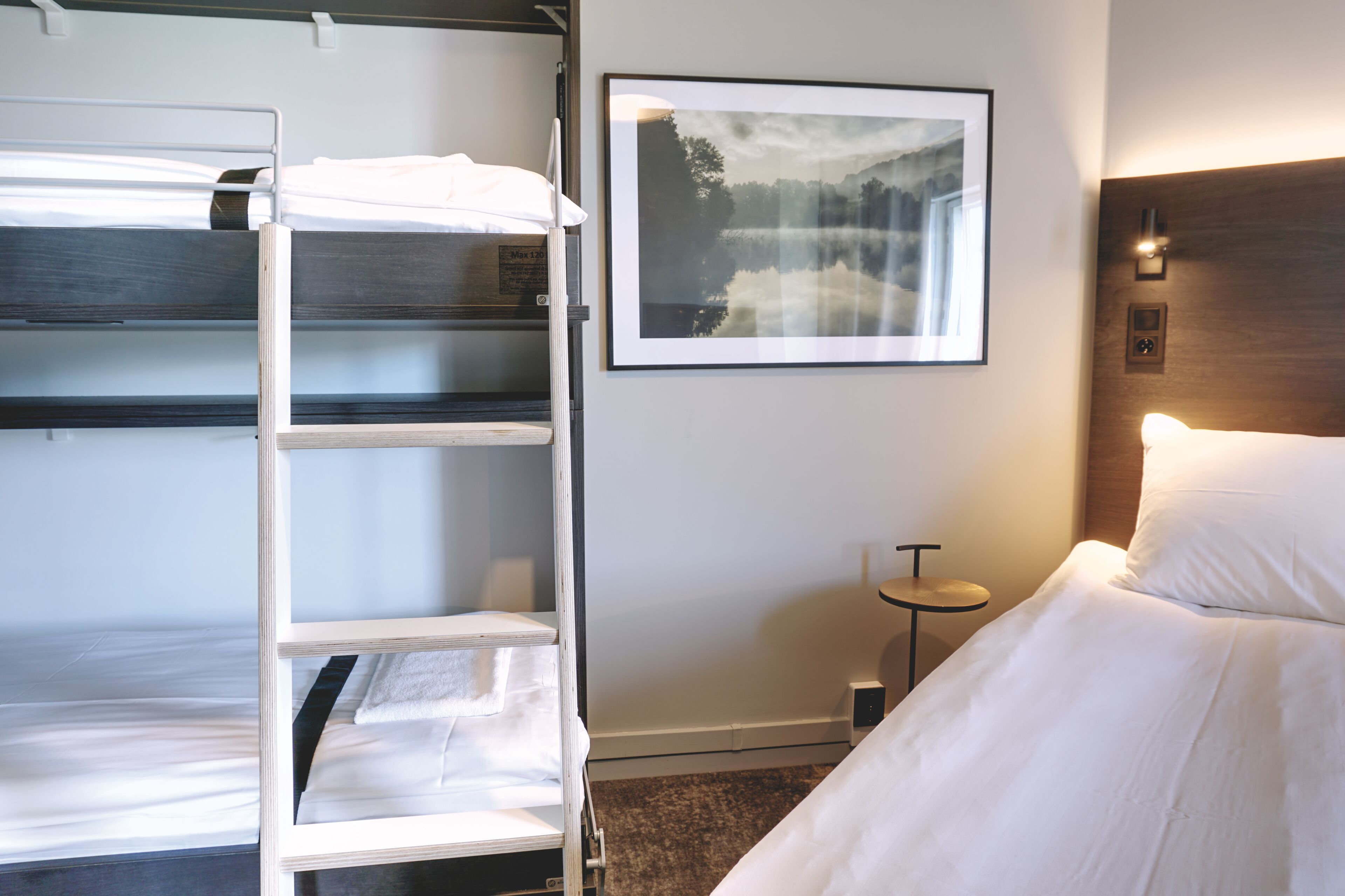 Een hotelkamer met stapelbedden, een ingelijste foto aan de muur, een nachtkastje en een bijzettafeltje.
