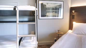 Una habitación de hotel con literas, un cuadro enmarcado en la pared, una mesita de noche y un velador.