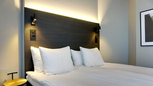A hotel room with a large bed, a small table, and a wall-mounted light fixture.