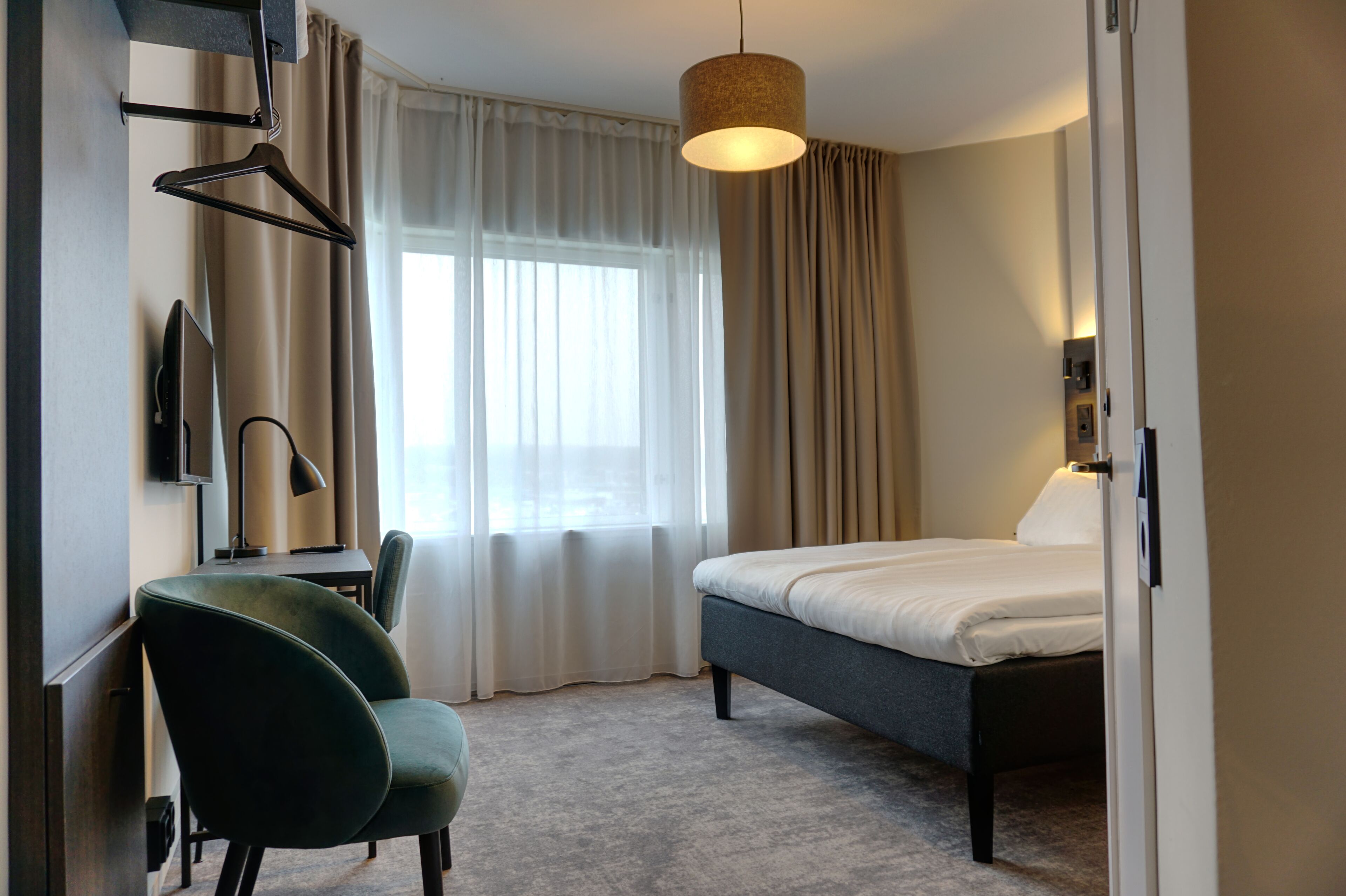 Een hotelkamer met een bed, een bureau met een stoel, een televisie en een lamp.