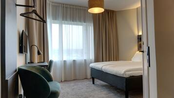 A hotel room with a bed, a desk with a chair, a TV, and a lamp.