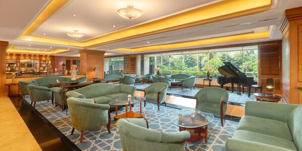 A spacious lobby with green upholstered chairs, a bar area, and a grand piano. - Aryaduta Menteng (Jakarta)