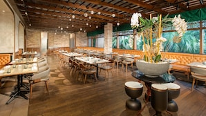 Un restaurante con una barra larga, mesas en cabinas y una gran maceta con orquídeas.
