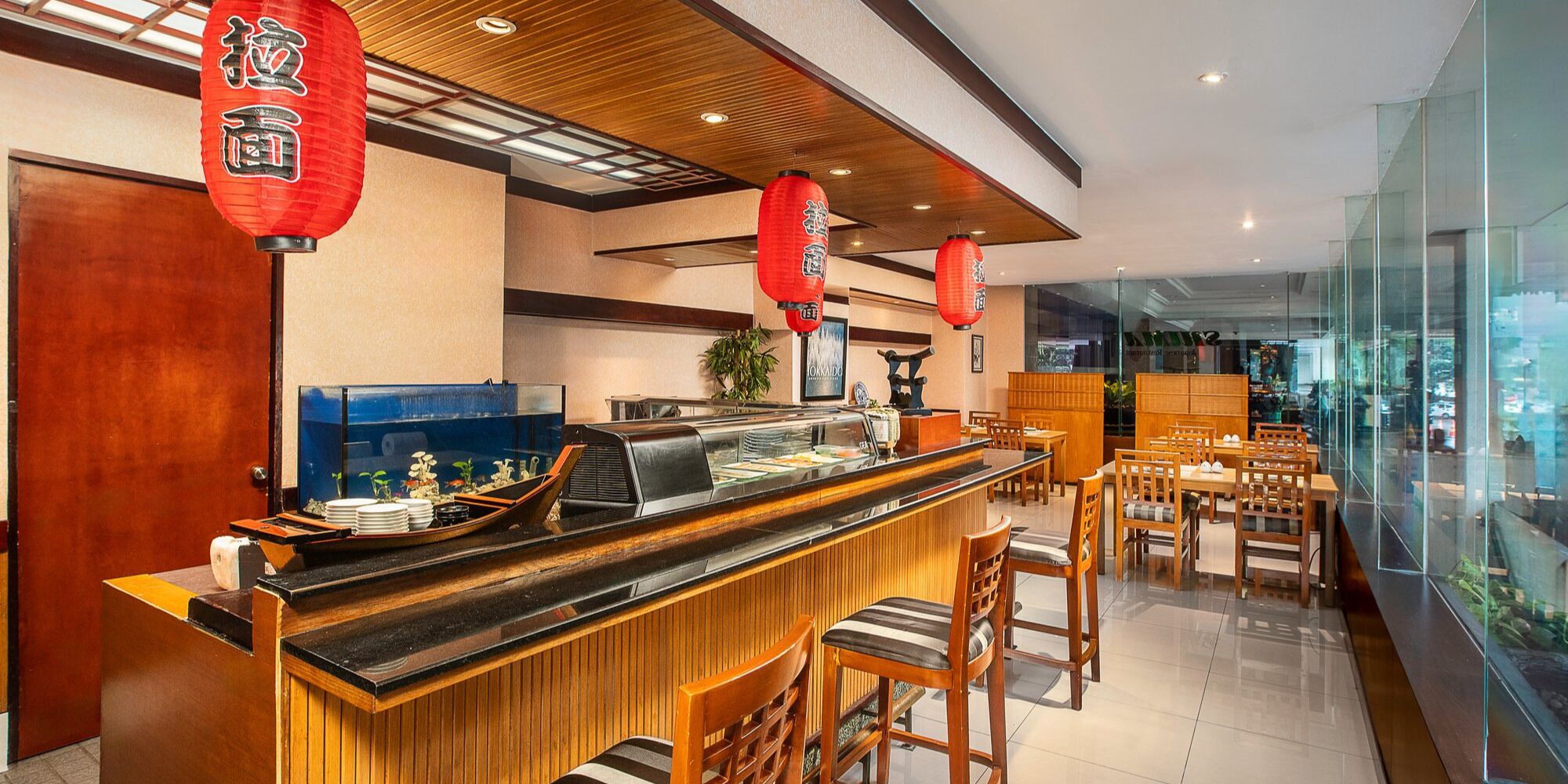 A restaurant with a wooden counter, red lanterns, and a view of the city through large windows.