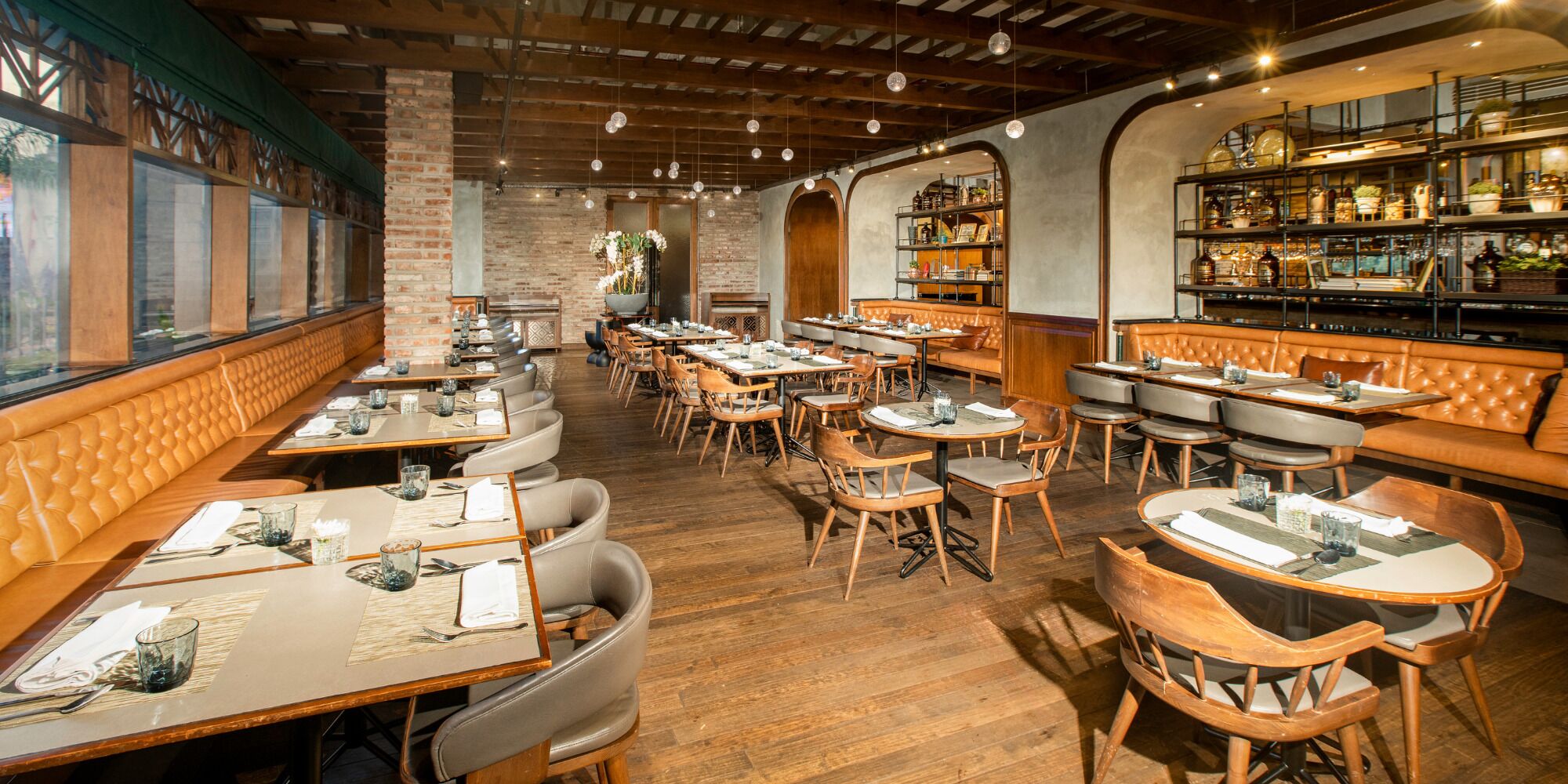 Un restaurant avec des tables et des chaises en bois, des murs en briques et un bar avec des étagères remplies de bouteilles.