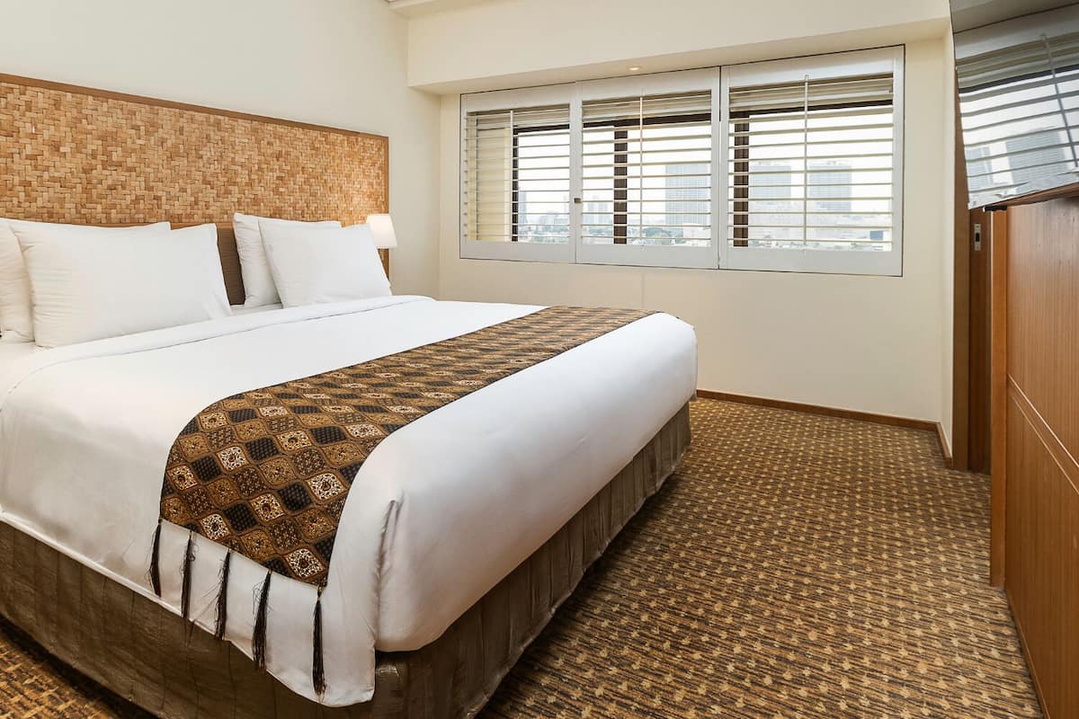 Ein Hotelzimmer mit einem großen Bett, einem Holz-Kopfteil, einem Fenster mit Jalousien und einem Schrank aus Holz.