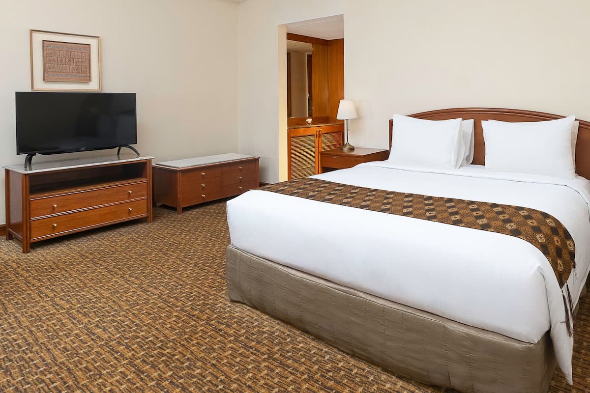 Ein Hotelzimmer mit einem großen Bett, einem Fernseher, einer hölzernen Kommode und einem Spiegel.
