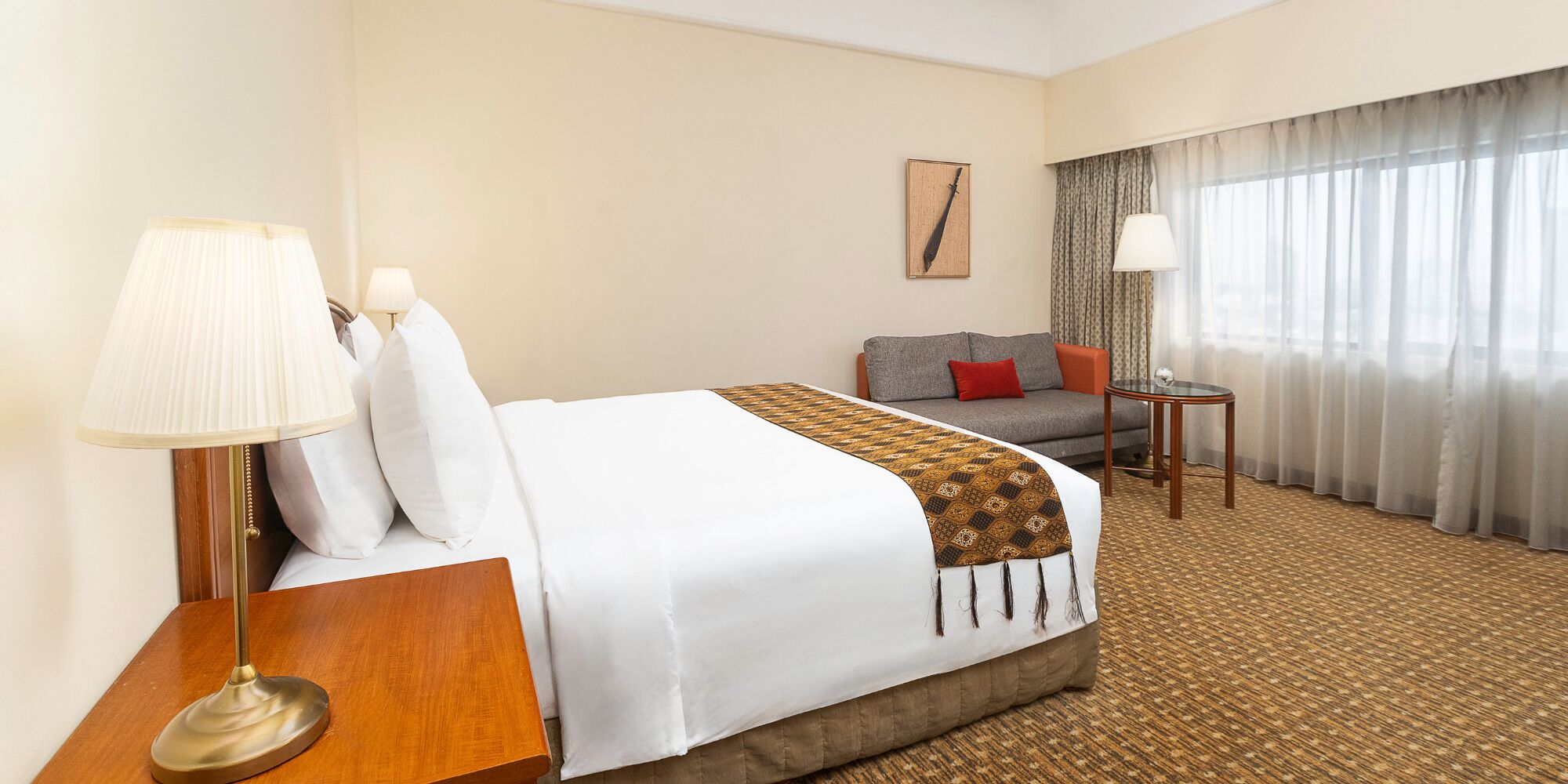 A hotel room with a bed, a sofa, a small table, a lamp, and a window with curtains.