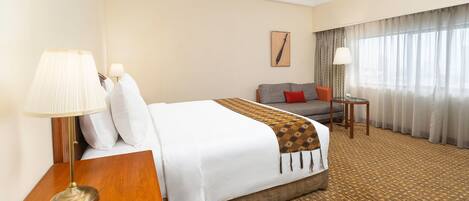 A hotel room with a bed, a sofa, a small table, a lamp, and a window with curtains.