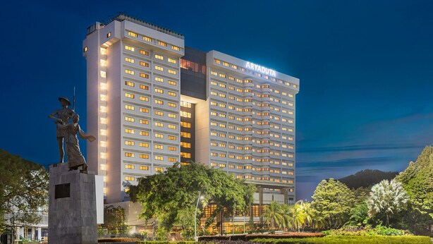 Un hotel de varios pisos con una estatua destacada en primer plano, rodeado de abundante vegetación.