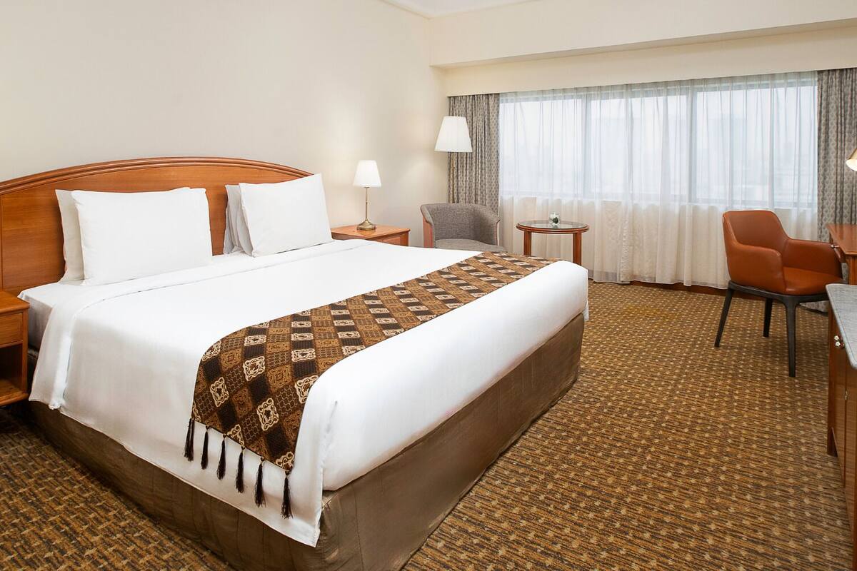 Ein Hotelzimmer mit einem großen Bett, zwei Nachttischen, einem Schreibtisch mit Stuhl, einem kleinen runden Tisch und einem Fernseher.