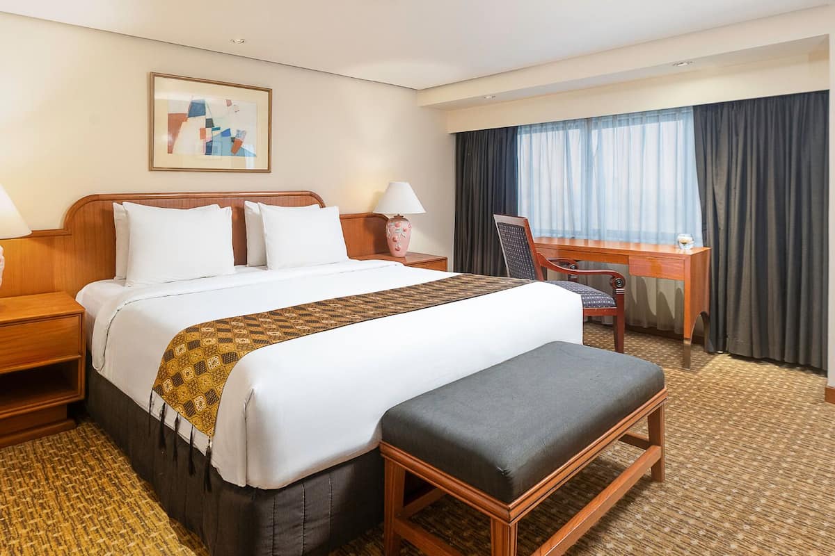 Ein Hotelzimmer mit einem großen Bett, zwei Nachttischen, einem Schreibtisch und einem Stuhl.