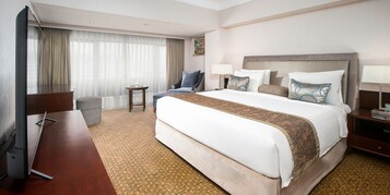 Una habitación de hotel con una cama grande, un escritorio, una silla, una mesita y una ventana con cortinas.