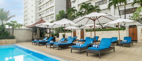 A poolside area with lounge chairs and umbrellas, a tiled deck, and a building in the background.
