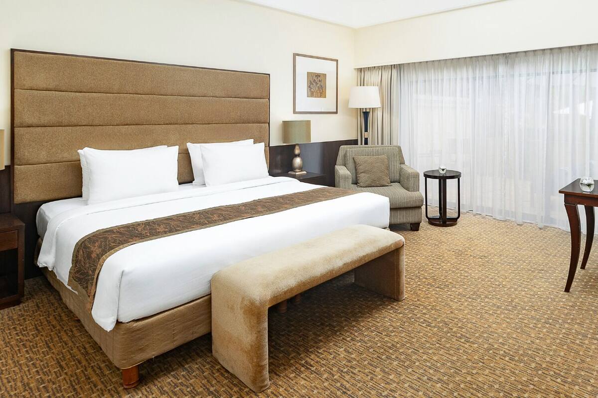 Ein Hotelzimmer mit einem großen Bett, einem Sessel, einem Tisch und einer Lampe.