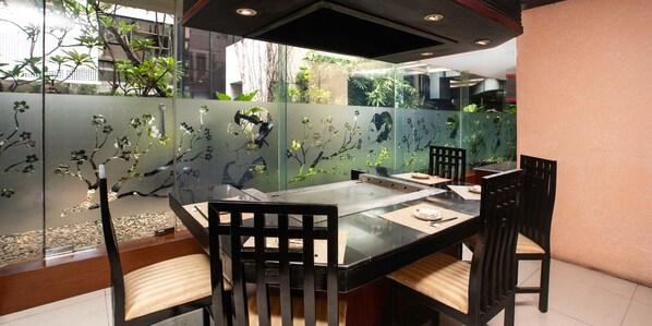A restaurant with a glass dining table, black chairs, and a view of greenery through a glass partition. - Aryaduta Menteng (Jakarta)