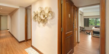 A hallway with wooden flooring, a decorative wall piece, and a wooden door leading to a room with a bed, a table, and a window.