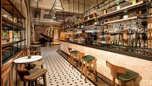 Un rincón de bar con piano, varios taburetes y una gran variedad de botellas y vasos en estanterías.