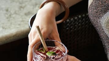 A close-up of a hand holding a glass with a straw, containing a beverage with ice and mint leaves.