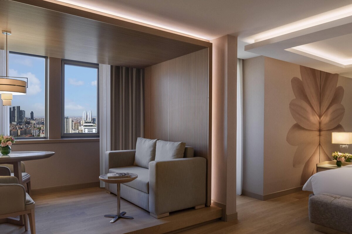 Habitación de hotel moderna con sofá, una mesita redonda, cama y ventana grande con vistas a la ciudad.