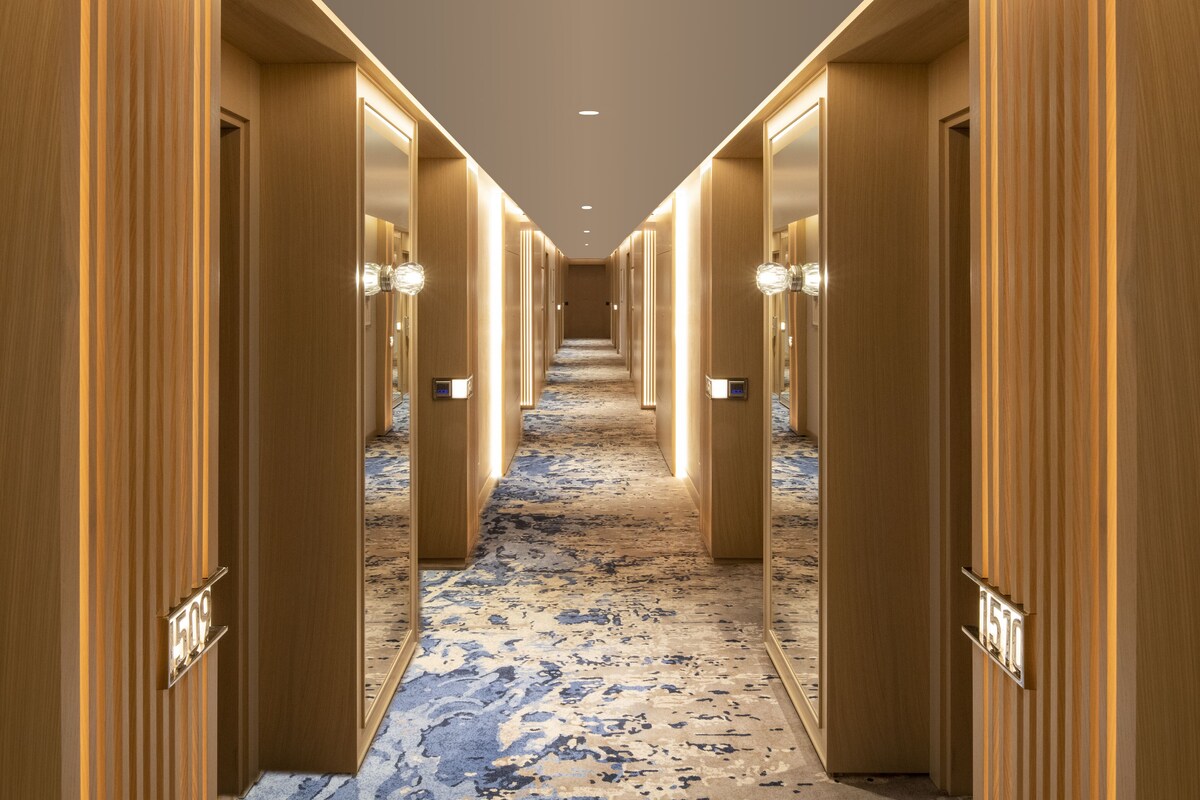 A hotel hallway with wooden paneling, numbered doors, and a patterned carpet.