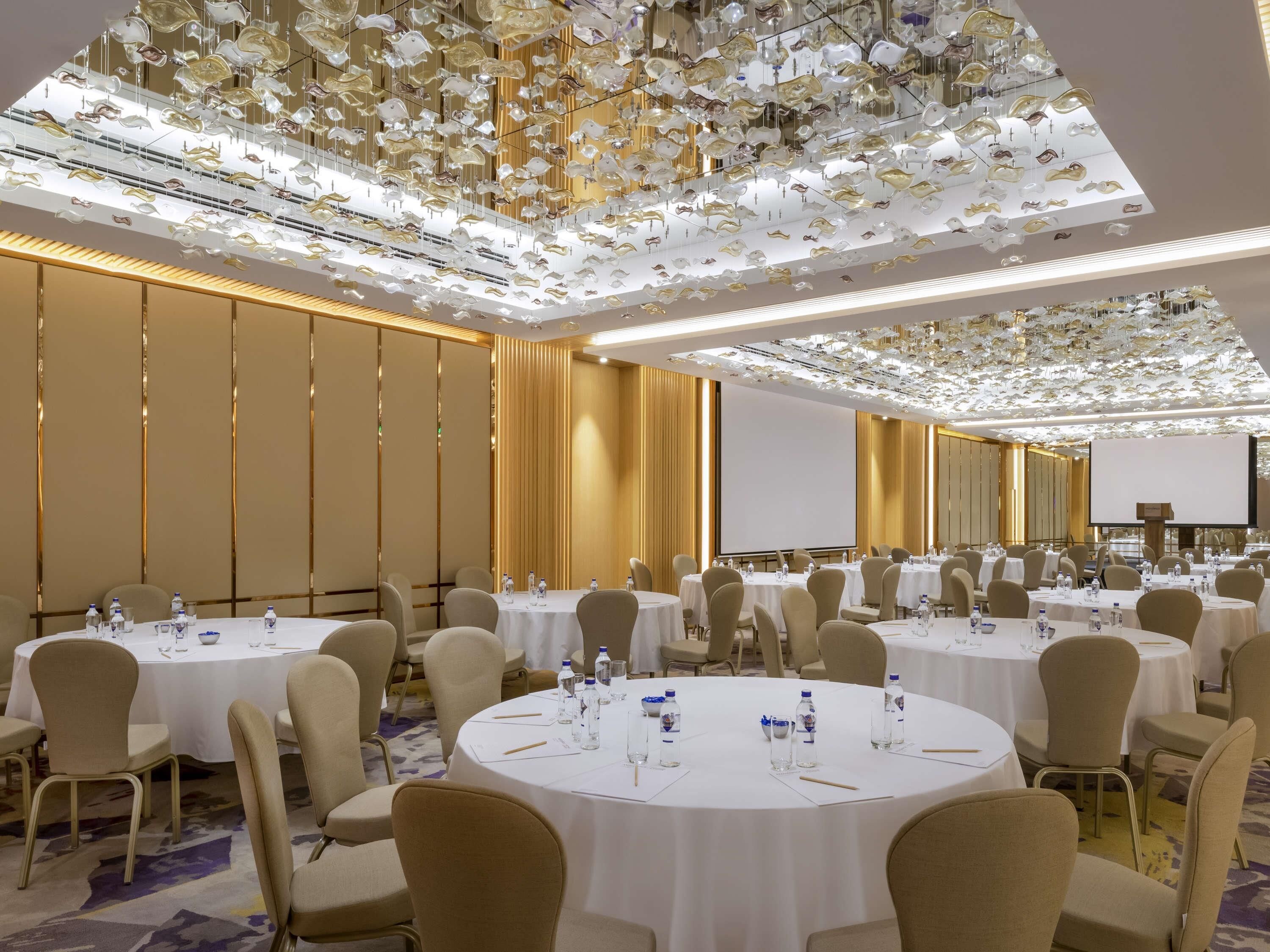 A conference room with round tables, chairs, water bottles, and a projector screen.