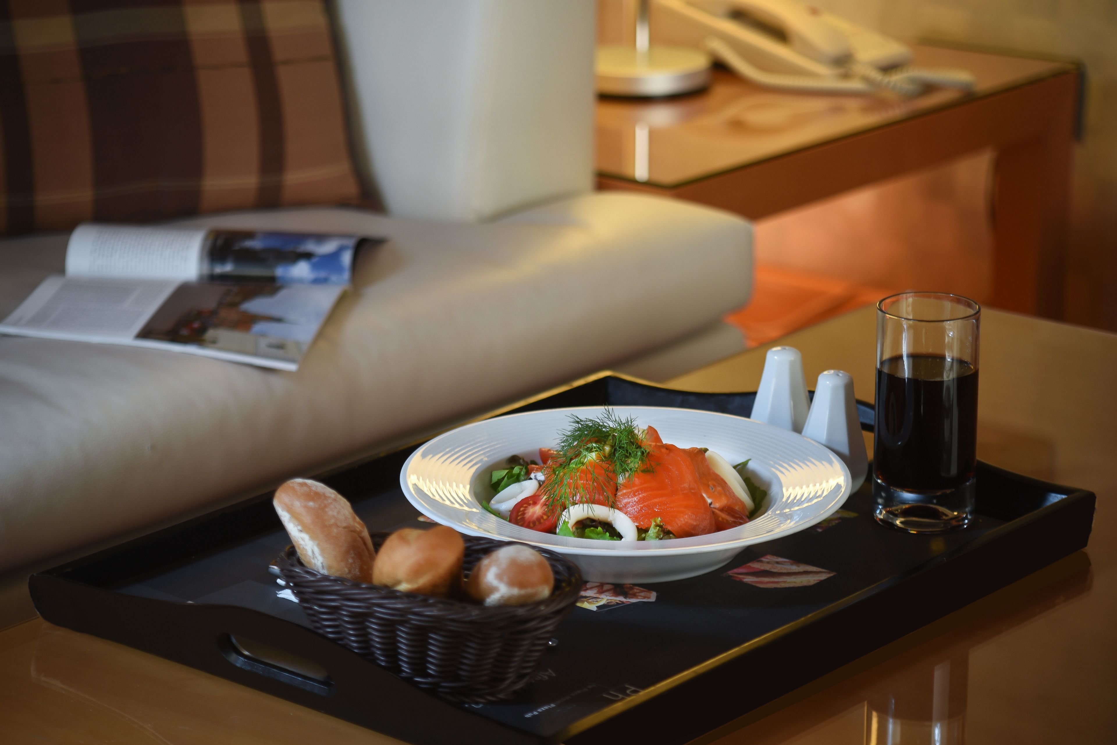 Een dienblad met een bord eten, een glas donker drankje en een broodmandje op een tafel in een hotelkamer.