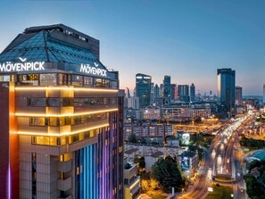 A modern building with 'MOVENPICK' signage, surrounded by a cityscape with high-rise buildings and a busy road.