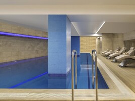 Una piscina con pared de azulejos, cubierta de madera y sillas de descanso.