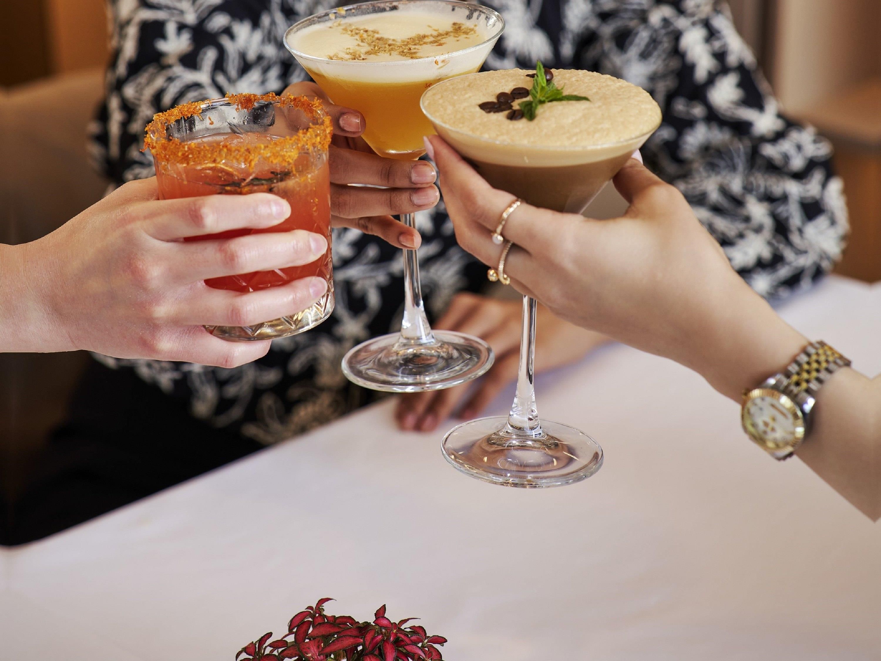Three people holding drinks at a table.