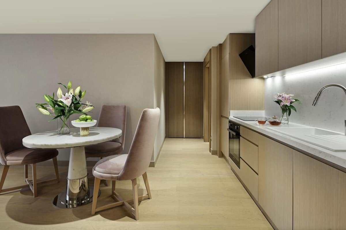 A modern kitchen with a dining area, featuring a round table, chairs, and a vase of flowers.