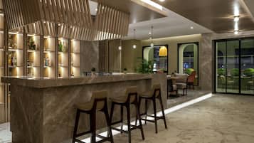 Zona de bar moderna amb taulell de marbre, tamborets i un panell decoratiu de fusta.