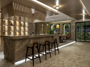 Un área de bar moderna con mostrador de mármol, taburetes y un panel decorativo de madera.