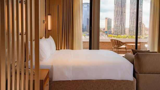 A hotel room with a large bed, a view of tall buildings, and a balcony with a chair. - Mövenpick Hotel Istanbul Bosphorus (Istanbul)