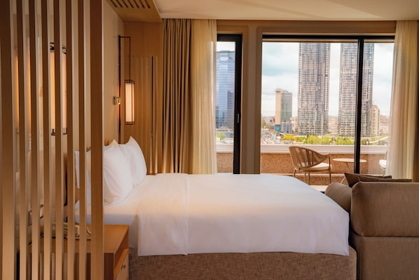 A hotel room with a large bed, a view of tall buildings, and a balcony with a chair. - Mövenpick Hotel Istanbul Bosphorus (Istanbul)