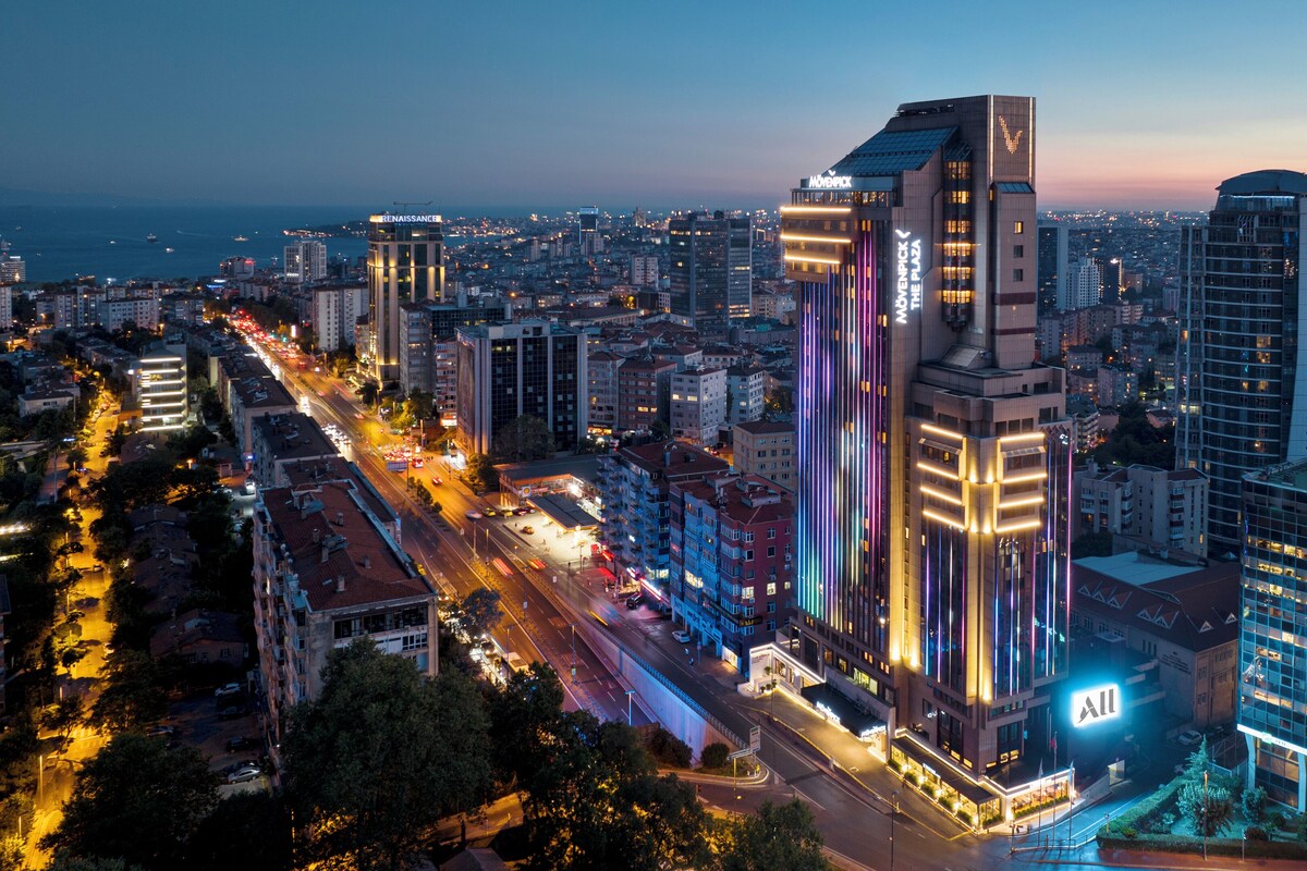 A cityscape with modern high-rise buildings, a busy street, and a prominent hotel with illuminated signage.