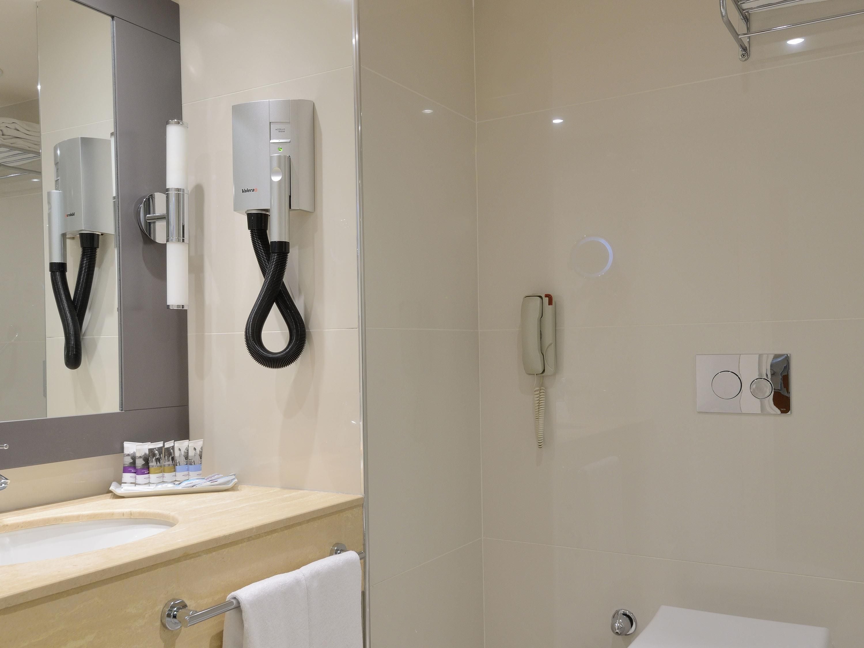 A modern bathroom with a sink, mirror, towel rack, and a hairdryer mounted on the wall.