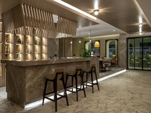 Uma área de bar moderna com bancada de mármore, banquetas e um painel decorativo de madeira.