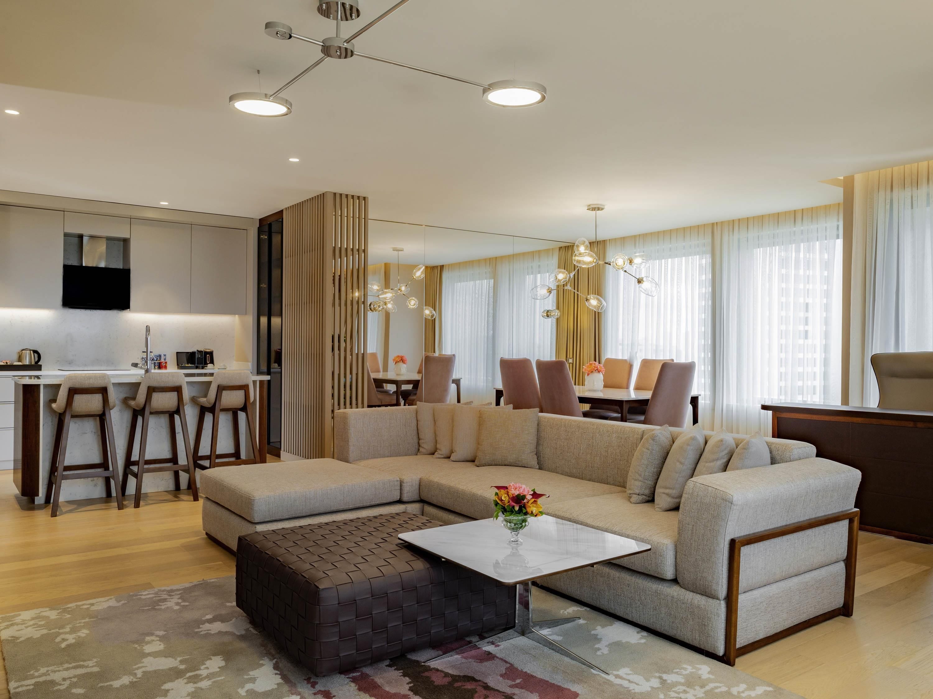 A modern living room with a sectional sofa, a coffee table, and a dining area in the background.