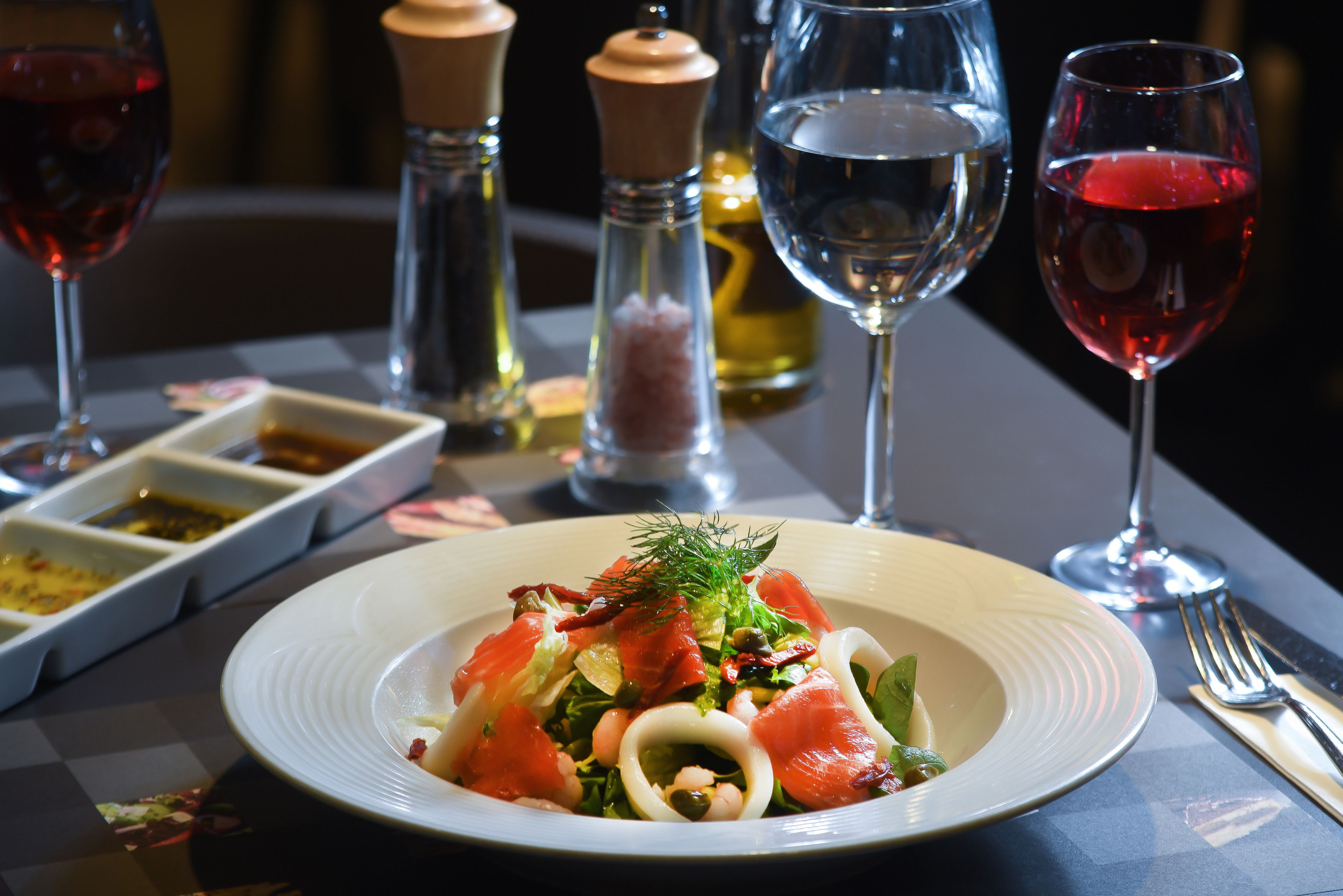 A table setting with a plate of food, two glasses of red wine, and salt and pepper shakers.
