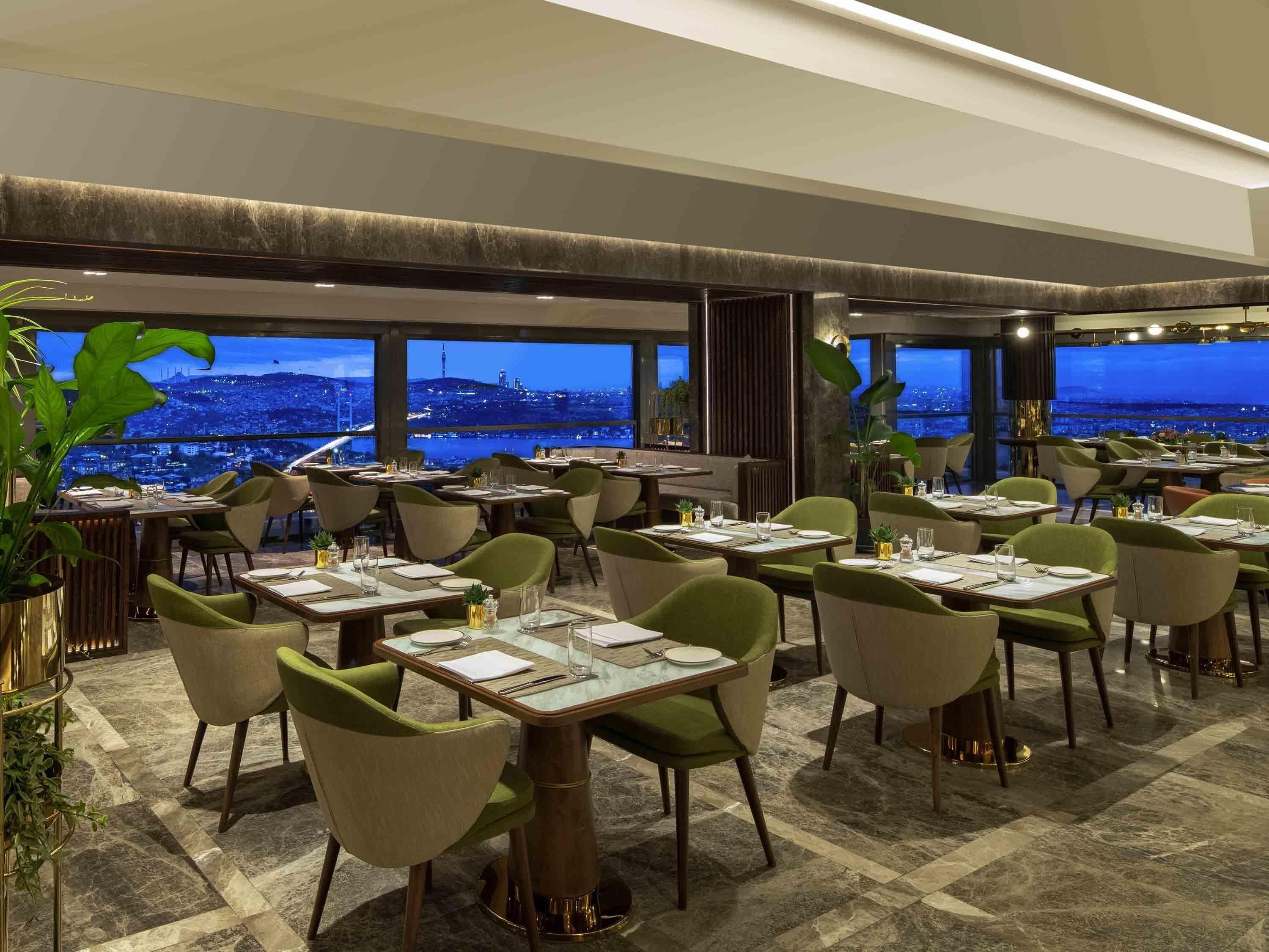 A restaurant with tables and chairs arranged for dining, large windows offering a city view, and a modern interior design.