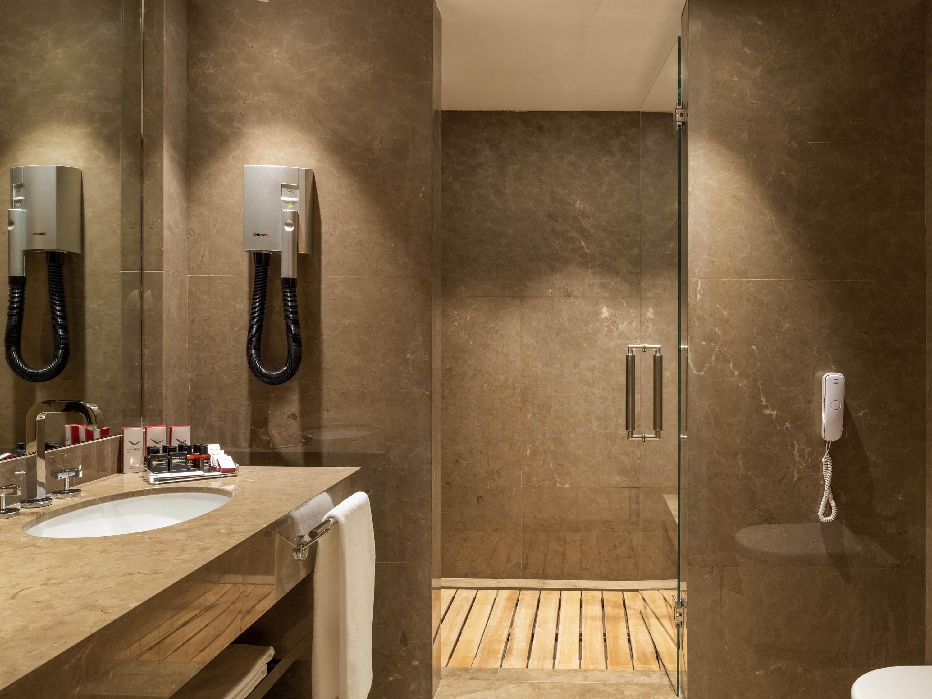 A modern bathroom with a glass shower enclosure, a vanity with a sink, and a telephone.