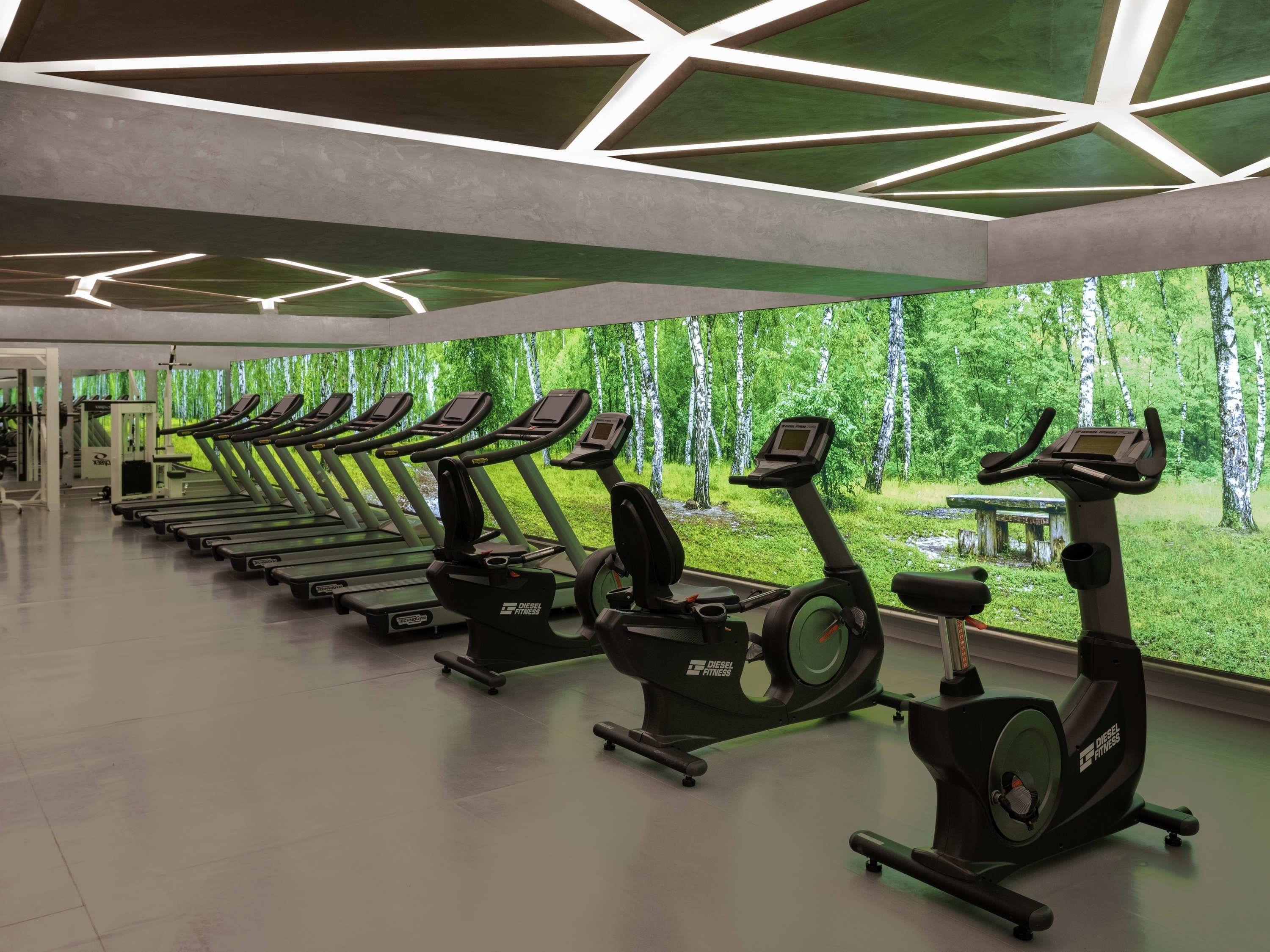 A gym with multiple treadmills and exercise bikes, a modern ceiling design, and a large window with a forest view.