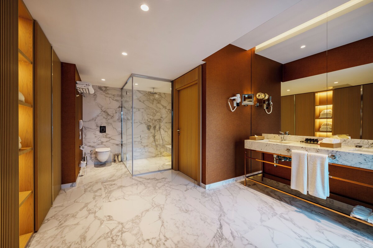 A modern bathroom with a marble floor, a large mirror, a shower, and a vanity with a towel rack.