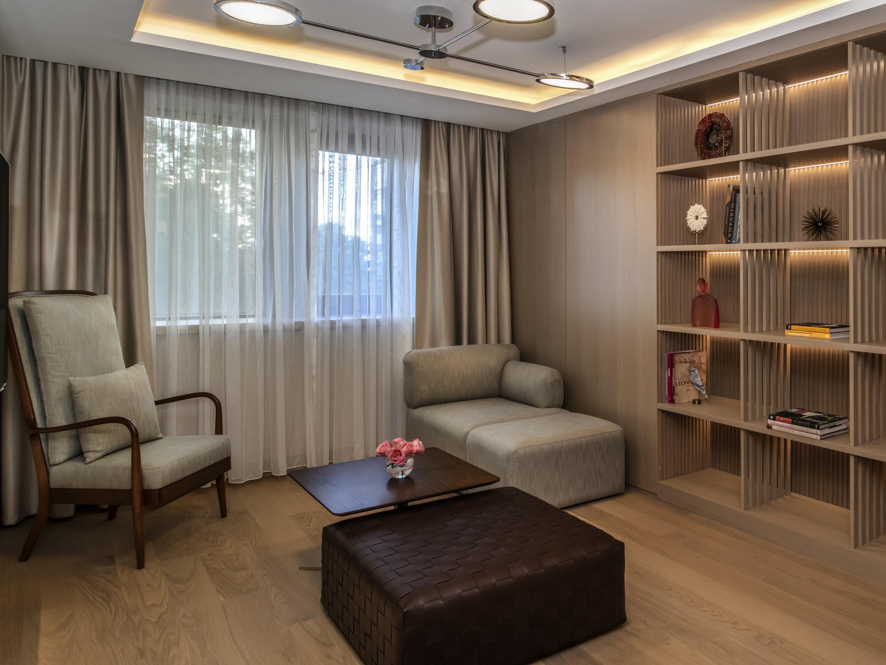 Una sala moderna con sofá, sillón, reposapiés y una estantería.