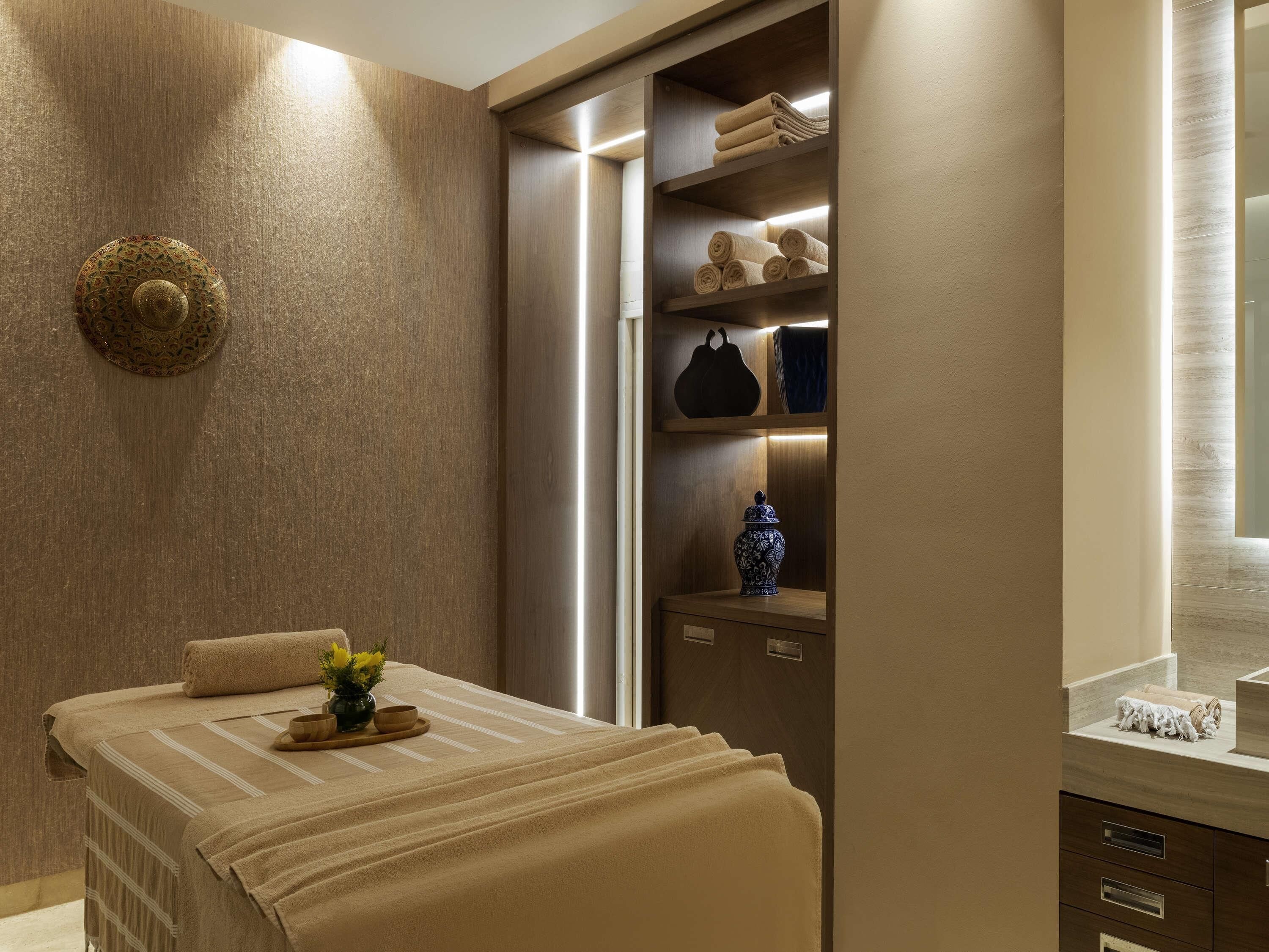 Een wellnessruimte met een bed, een plank met handdoeken en een decoratief wandobject.