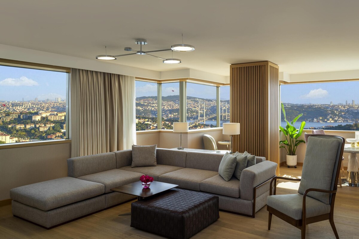 Una sala moderna con un sofá modular, una mesa de centro y vistas de un paisaje urbano a través de amplios ventanales.