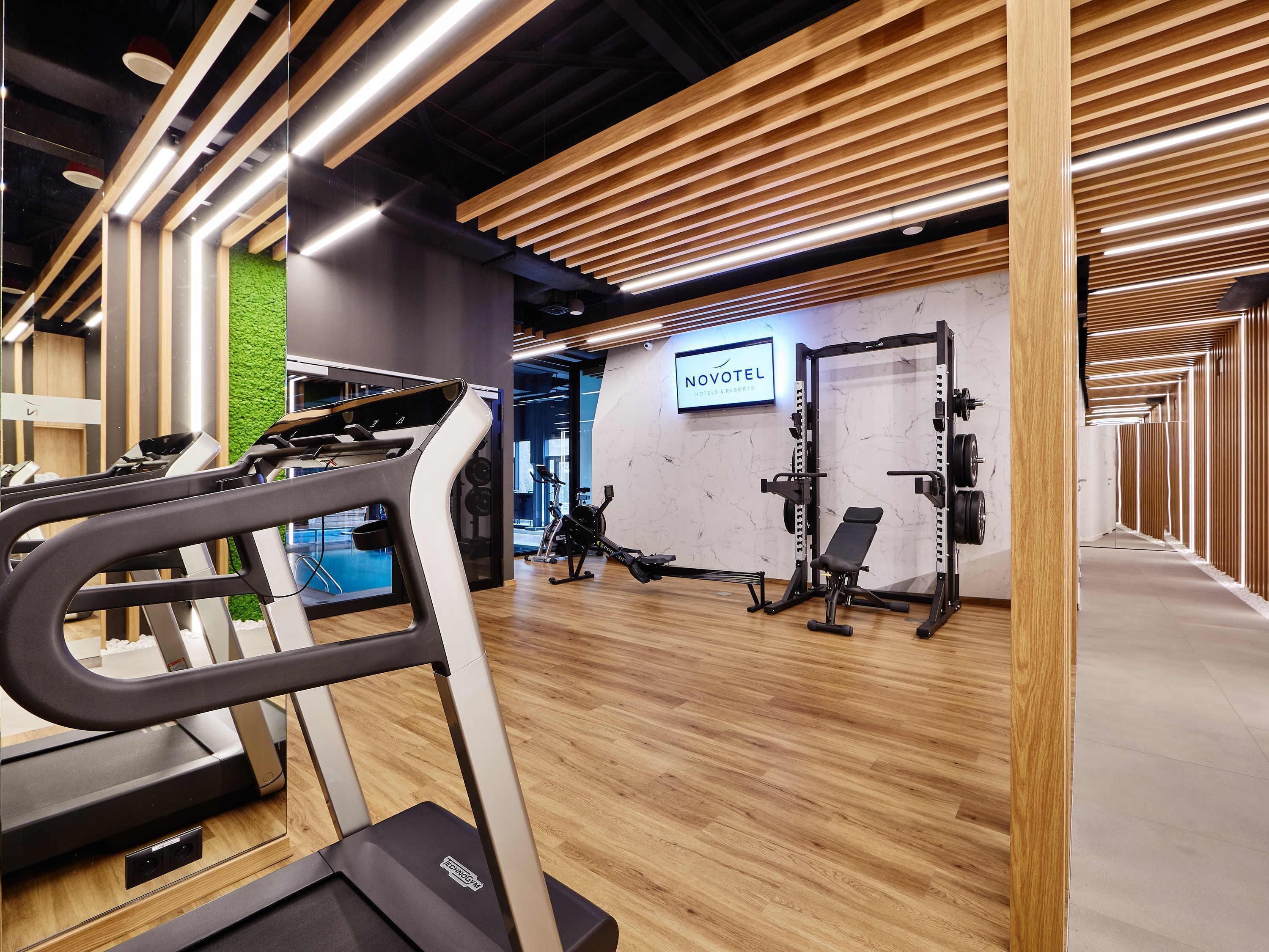 Een moderne sportschool met loopbanden, een krachtapparaat en een groene wand.