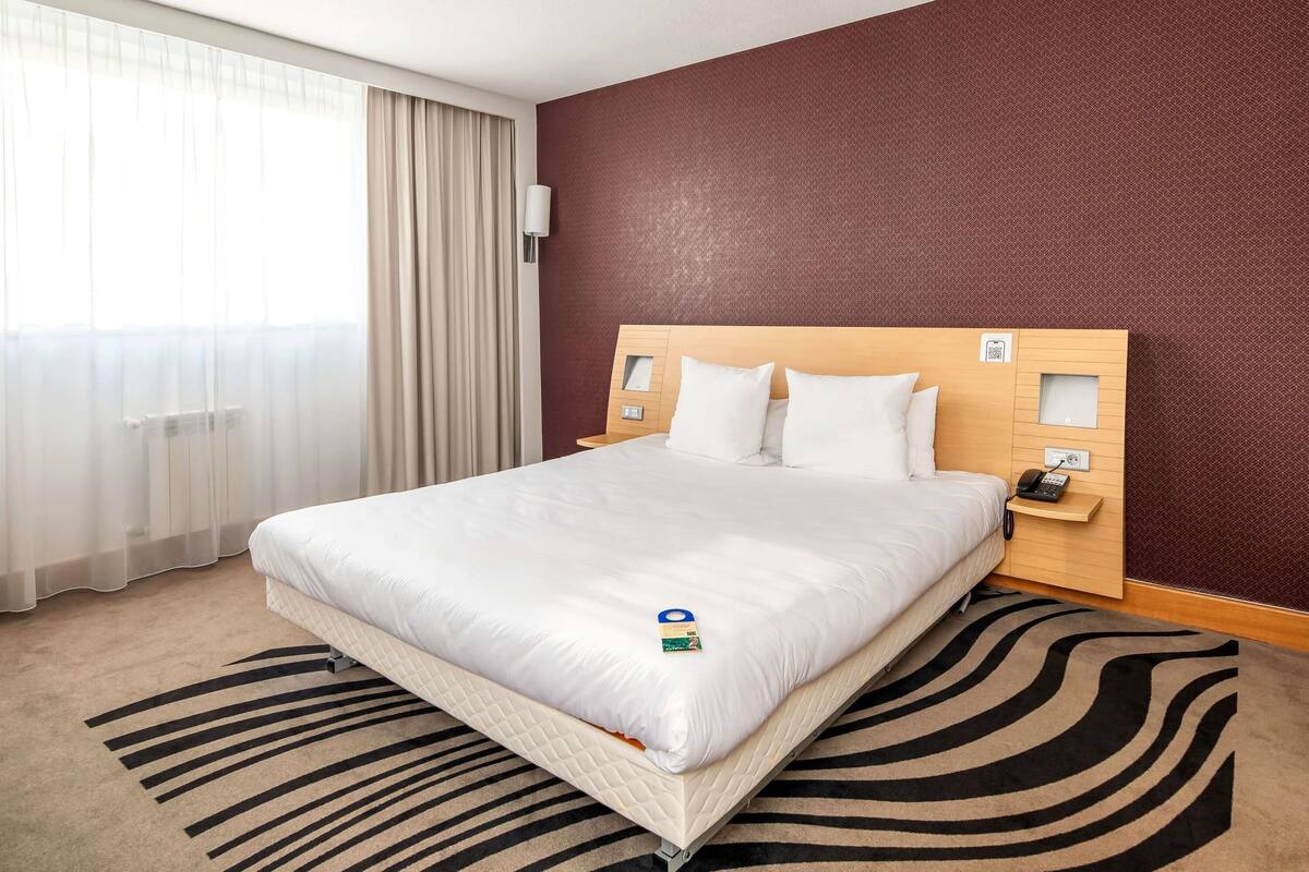 Een hotelkamer met een bed, nachtkastje, telefoon en raam met gordijnen.